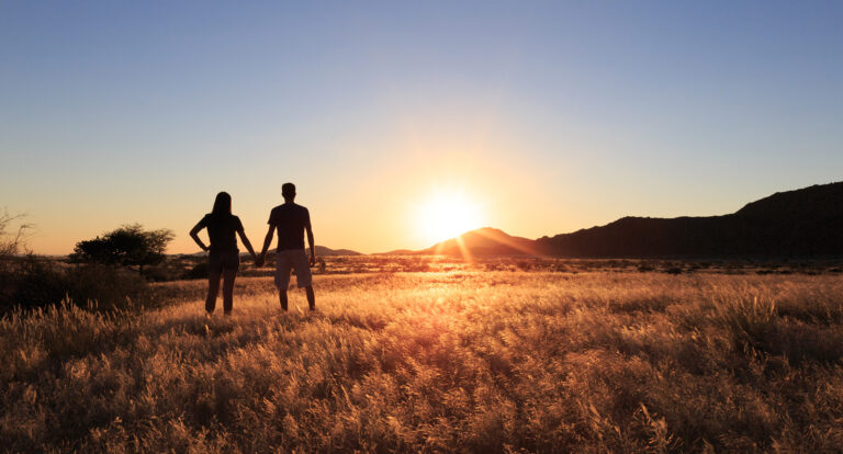 People standing in a field watching the sunset at the Bagatelle Kalahari Game Ranch.