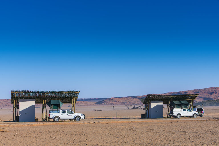 Two of the Sesriem Oshana Camping areas with vehicles parked underneath them.